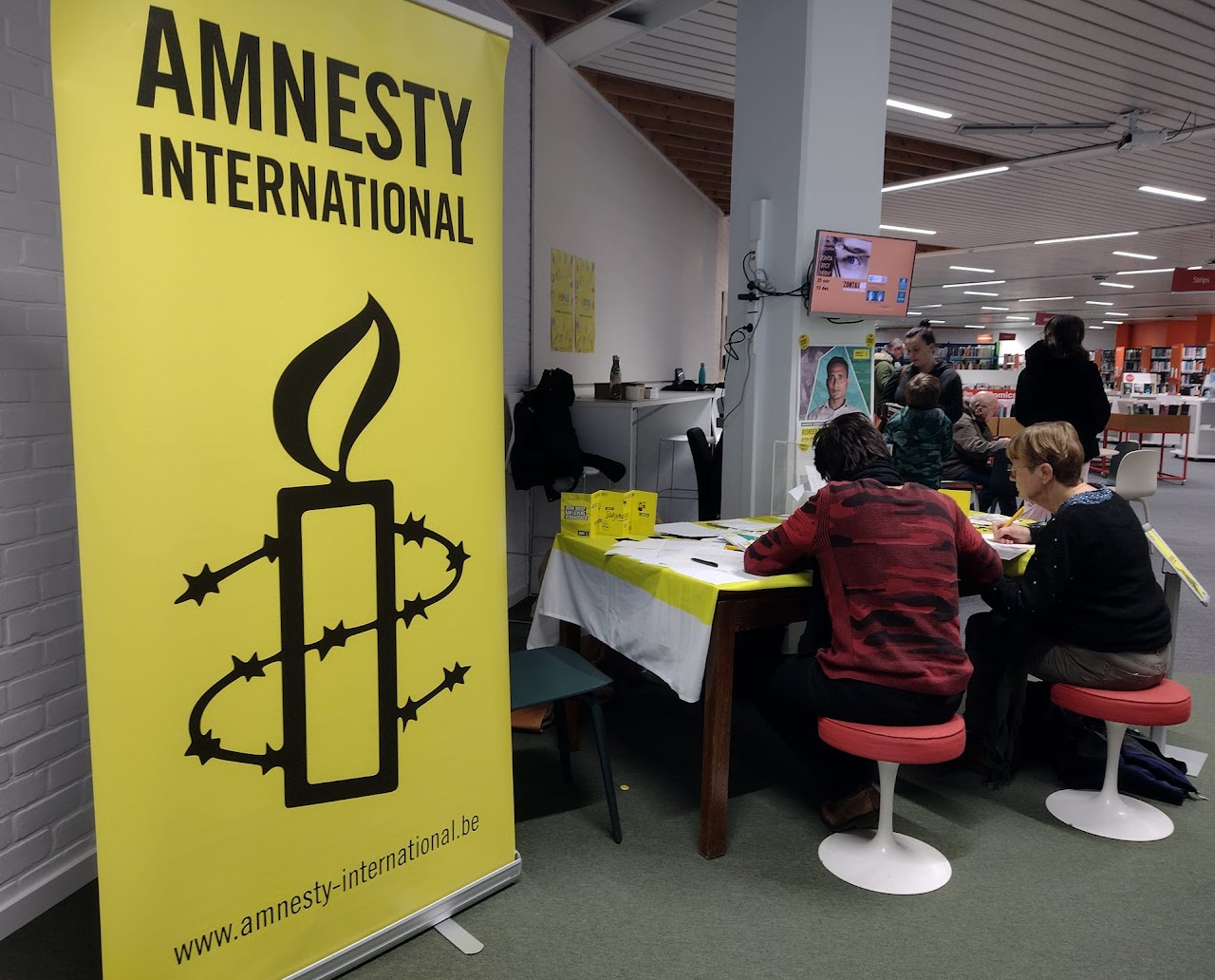 Doe je mee? Een grote banner van Amnesty International met een tafel naast en twee mensen die zich aan het inschrijven lijken te zijn